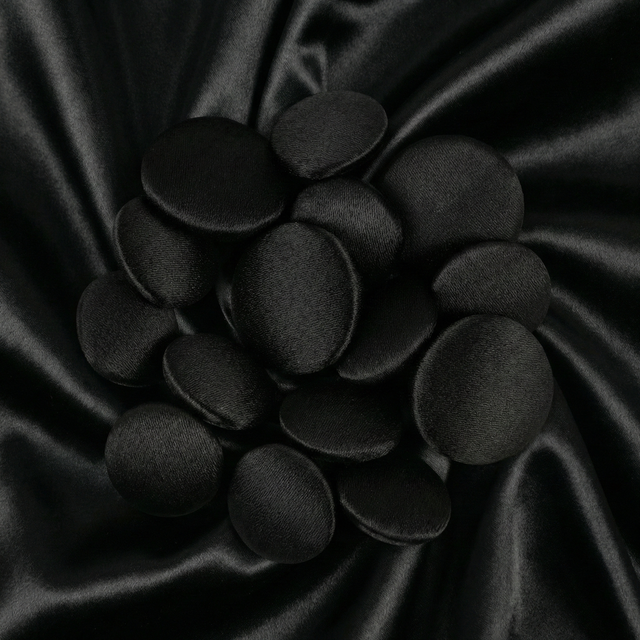 Tuxedo Suit Buttons in shiny black satin, artfully arranged on smooth black satin fabric with gentle, wavy folds.