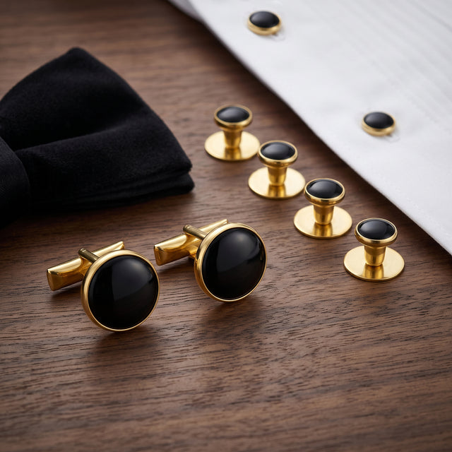 Tuxedo Shirt Studs and Cufflinks in gold and black are displayed on a wooden surface, accompanied by a classic tuxedo shirt and a black bow tie.