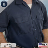 A man wearing a dark blue short-sleeve button-up shirt with two chest pockets displays a visible “Made in USA” label and features Work Shirt Buttons manufactured to military specifications for enhanced durability and long-lasting wear.