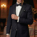 A man wearing a black tuxedo with Tuxedo Suit Buttons and a bow tie stands indoors, adjusting his jacket in an elegant setting.