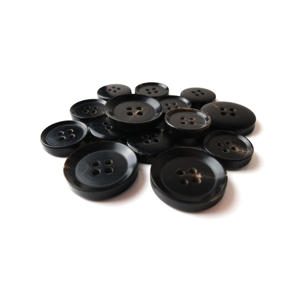 A pile of Buffalo Horn Suit Buttons, all black with four holes, arranged on a white background.