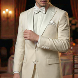 A man at a formal indoor event wears a white tuxedo with black satin Tuxedo Suit Buttons and a bow tie.