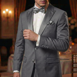 A man in a gray tuxedo and bow tie stands indoors against an elegant, softly lit backdrop, his look elevated by Tuxedo Suit Buttons.