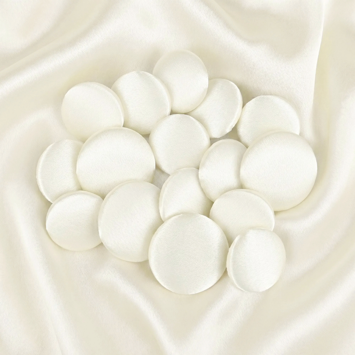 Tuxedo Suit Buttons: Round white satin fabric pads arranged on smooth ivory satin fabric, reminiscent of elegant formalwear details.