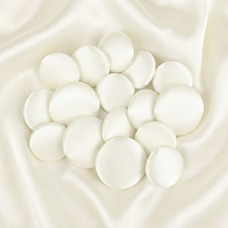 Tuxedo Suit Buttons: Round white satin fabric pads arranged on smooth ivory satin fabric, reminiscent of elegant formalwear details.