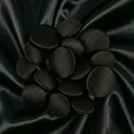 Tuxedo Suit Buttons in shiny black satin, artfully arranged on smooth black satin fabric with gentle, wavy folds.