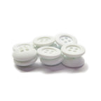 A pile of small white Rubber Shirt Buttons with four holes, scratchproof, scattered on a white surface—ideal for children's clothing.