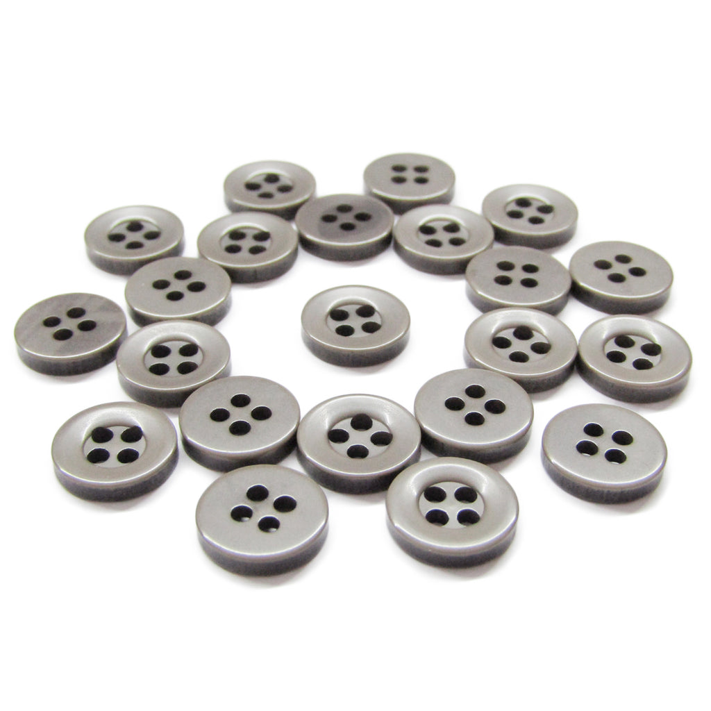 Several Workshop Uniform Shirt Buttons, small, round, gray, and made of durable nylon with four holes, are scattered on a white surface.
