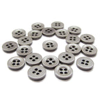 Several Workshop Uniform Shirt Buttons, small, round, gray, and made of durable nylon with four holes, are scattered on a white surface.