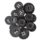 A scattering of Vegan Faux Horn Suit Buttons, each black with four holes, displayed against a white background.