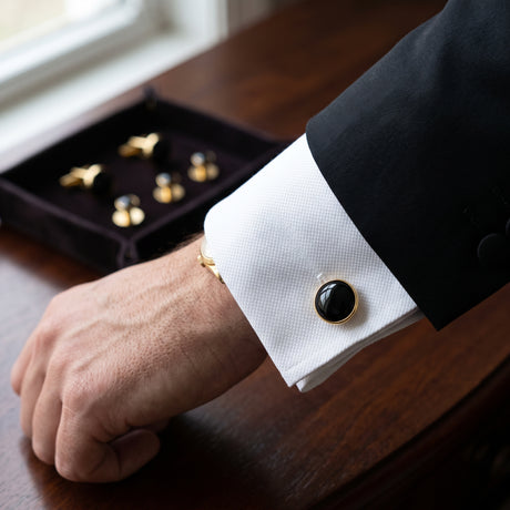 A person in a suit wears a white shirt accented with the Tuxedo Shirt Studs and Cufflinks, displayed near their box.