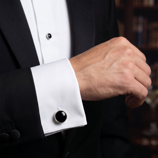 A man in a black tuxedo adjusts his Tuxedo Shirt Studs and Cufflinks on a white dress shirt, with only his hand and arm visible.