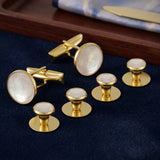 Tuxedo Shirt Studs and Cufflinks, crafted from gold and mother-of-pearl, are showcased on dark blue fabric with a wooden tray—an ideal accessory set for your tuxedo shirt.