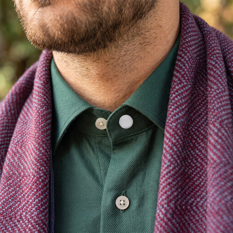 A close-up of a man wearing a green shirt and a purple herringbone scarf, showing only his neck and chin, with the perfect fit achieved using Collar Extenders.