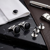 Tuxedo Shirt Studs and Cufflinks with black centers rest elegantly on a marble surface, paired with a white shirt and pen—these stainless steel accessories are the perfect addition to any formal tuxedo ensemble.