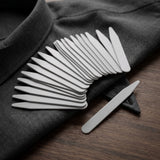 A collection of Collar Stays is arranged on a gray suit jacket, with one Collar Stay set apart.