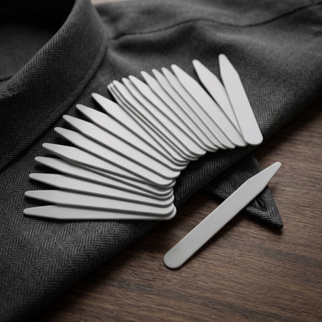 A collection of Collar Stays is arranged on a gray suit jacket, with one Collar Stay set apart.