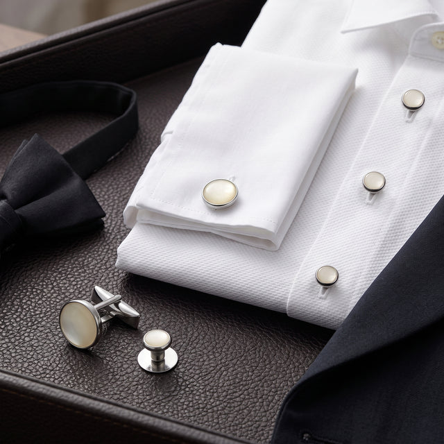 A white dress shirt accented with the Tuxedo Shirt Studs and Cufflinks, a black bow tie, and a dark suit jacket on a leather surface—an elegant ensemble elevated by these sophisticated tuxedo shirt accessories.