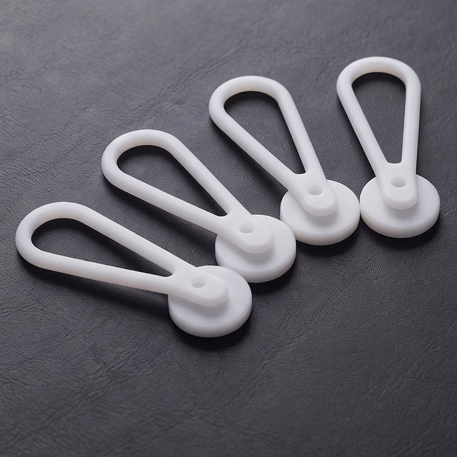 Four teardrop-shaped, white plastic Collar Extenders—perfect for expanding your collar size—are arranged on a dark textured surface.