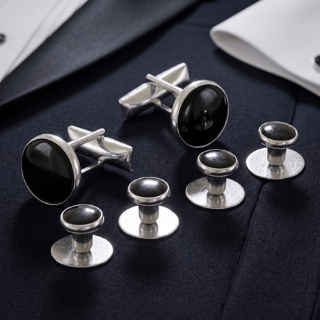 The Tuxedo Shirt Studs and Cufflinks, featuring sleek silver with black centers, add an elegant touch to a white dress shirt and navy suit.