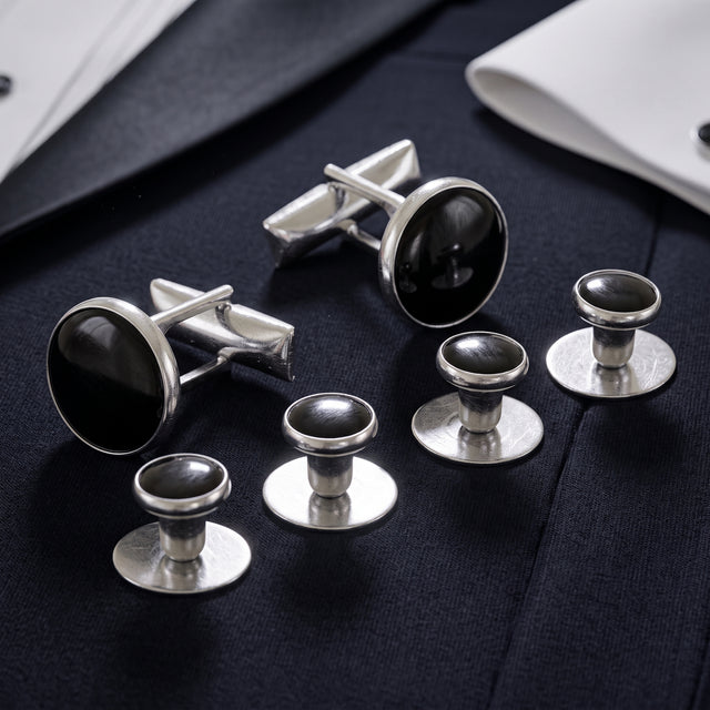 The Tuxedo Shirt Studs and Cufflinks, featuring sleek silver with black centers, add an elegant touch to a white dress shirt and navy suit.