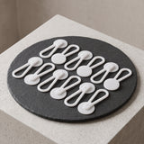 Twelve Collar Extenders are arranged neatly on a round black slate atop a light stone surface.