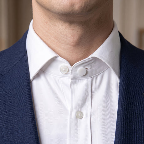 A close-up of a person wearing a blue suit and white shirt with a collar pin attached, enhanced for comfort with discreet Collar Extenders.