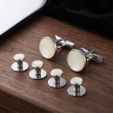 Tuxedo Shirt Studs and Cufflinks, featuring white insets, are displayed on a wooden surface beside black fabric—ideal accessories for a tuxedo shirt.