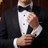 A man in a black tuxedo adjusts his stainless steel Tuxedo Shirt Studs and Cufflinks and bow tie, dressed formally for an event with sophisticated tuxedo shirt accessories.